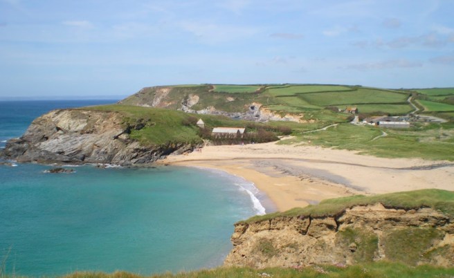 Sandy beach enclosed by green field headlands, clear blue water under a blue sky.