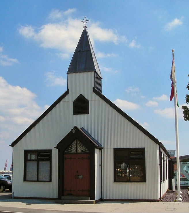 Simple black and white church with small black Nordic spire, and flagpole adjacent to the church.