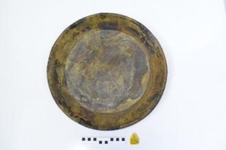 Pan after cleaning, with concretion removed, showing a darker metal colour and some discolouration. Scale rule and yellow tag below.