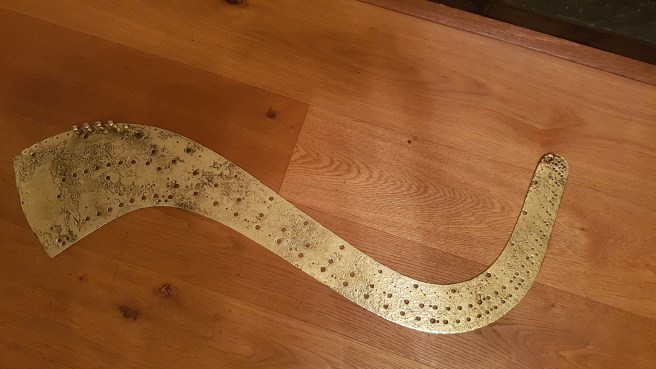 Curved metal plate with pegs and holes on a wooden table.