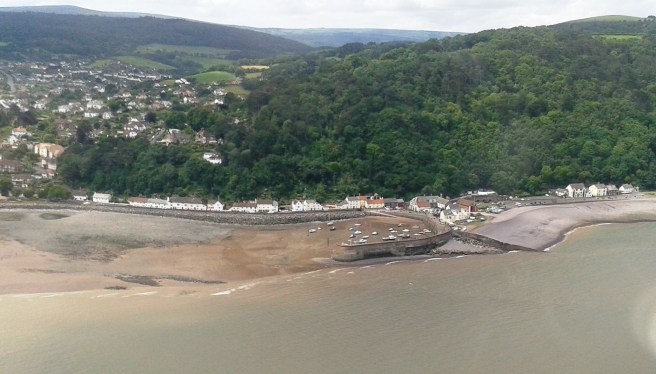 View of sea to bottom of image, beach at centre left to middle, with town and green wooded area to background of image.