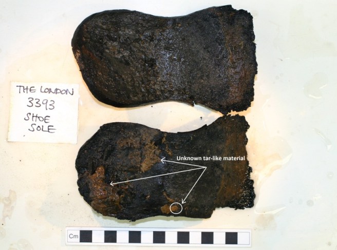 Two shoe soles one below the other, against a white background, and a centimetre scale rule underneath. Annotated on the lower sole where unknown tar-like materials have been seen.