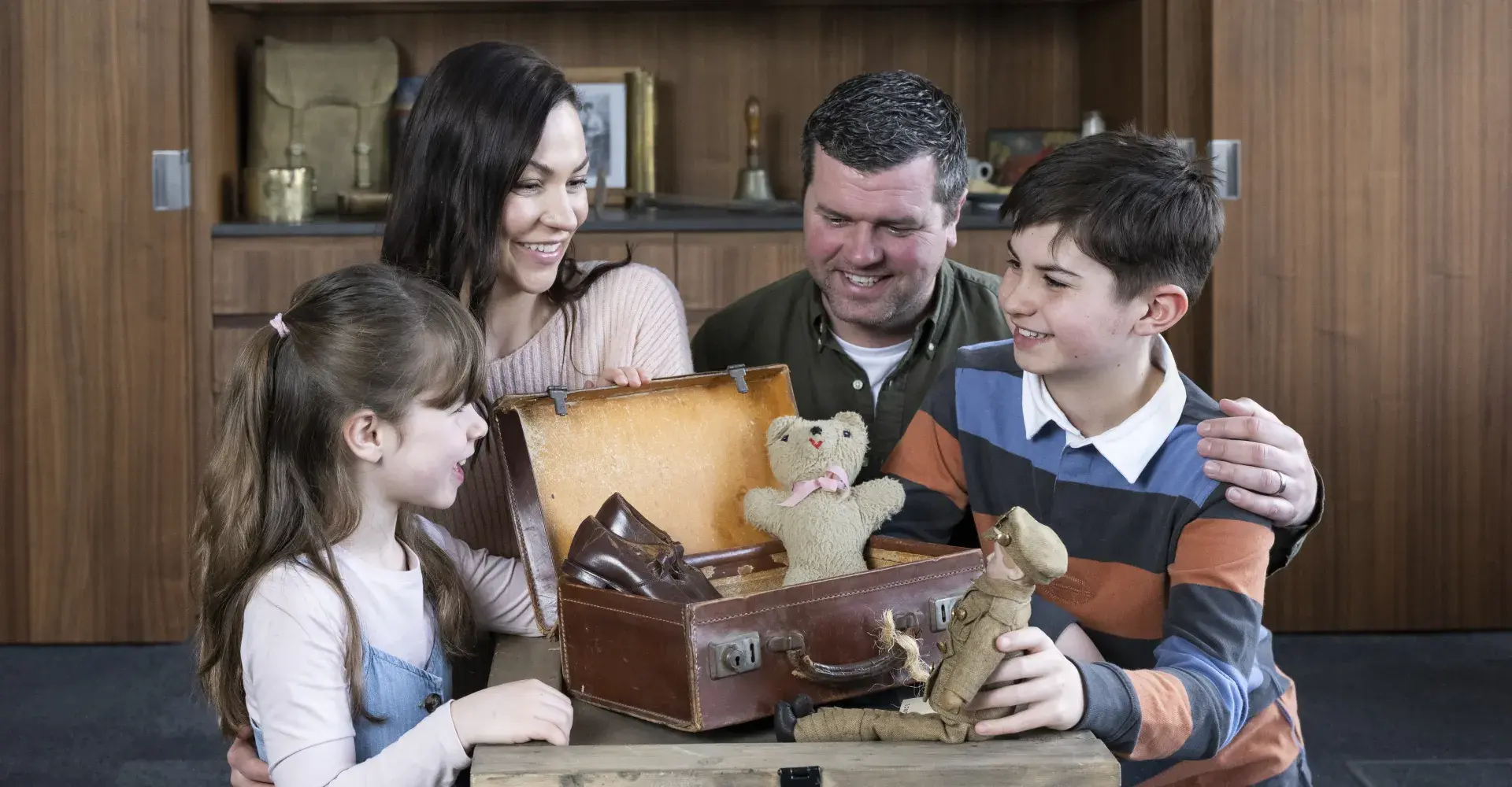 A family examines a suitcase featuring IWM collections items including a toy solider and soft toy bear