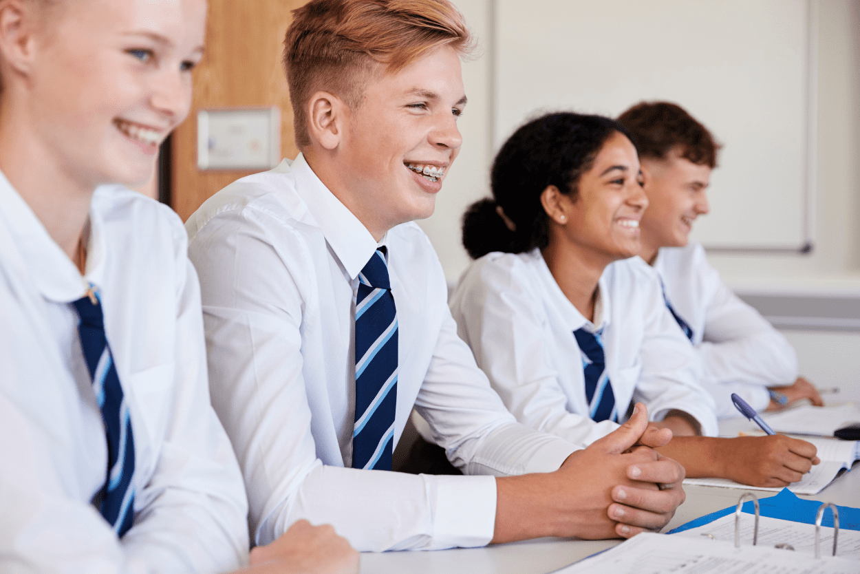 Four secondary school students smiling at a desk wearing school uniform