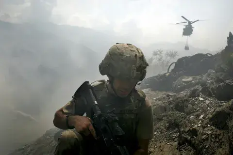 A soldier turns away from a dust cloud being created by a helicopter that is hovering above an outpost in Afghanistan.