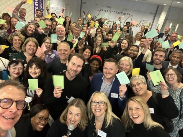 A large group of people smile at the camera and hold coloured cards up.