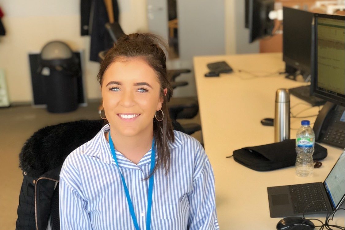 Industrial placement Jess Johnson sitting at her desk with a laptop and smiling