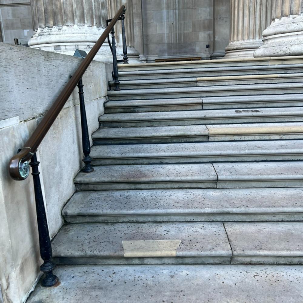 11 stone steps with a metal handrail on the left. The bases of three large stone pillars are in view at the top. 