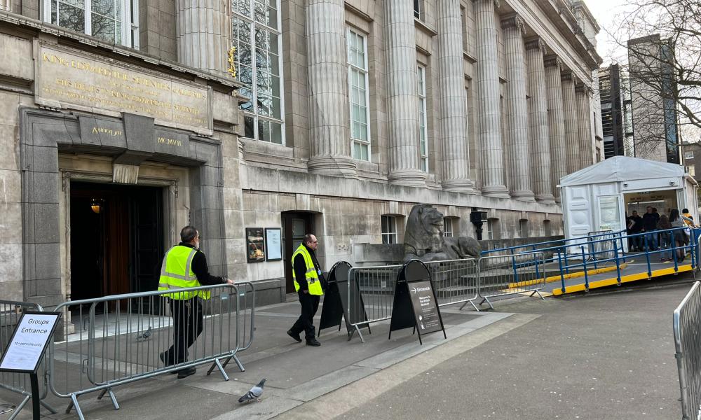 Two security guards stand next to metal barriers outside the Montague Place entrance, with a security tent on the right.  