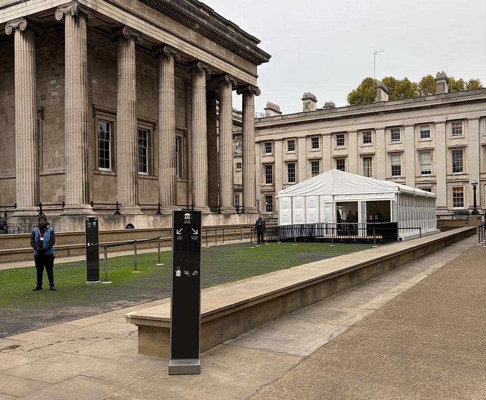 View of the right-hand side of the British Museum forecourt, showing stanchions leading to a white security pavilion.