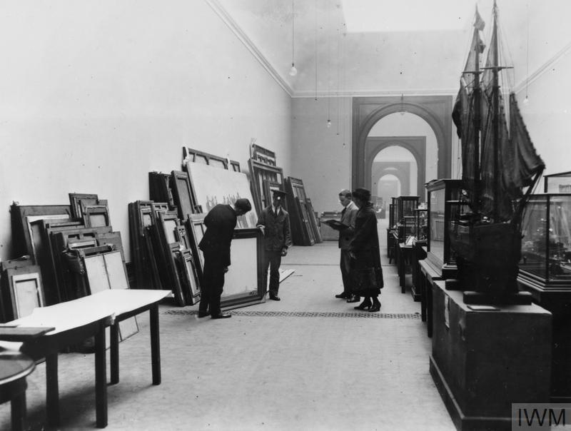 A group of Imperial War Museum staff inspect frames stacked against a wall, while remounting the museum's displays in South Kensington in 1924