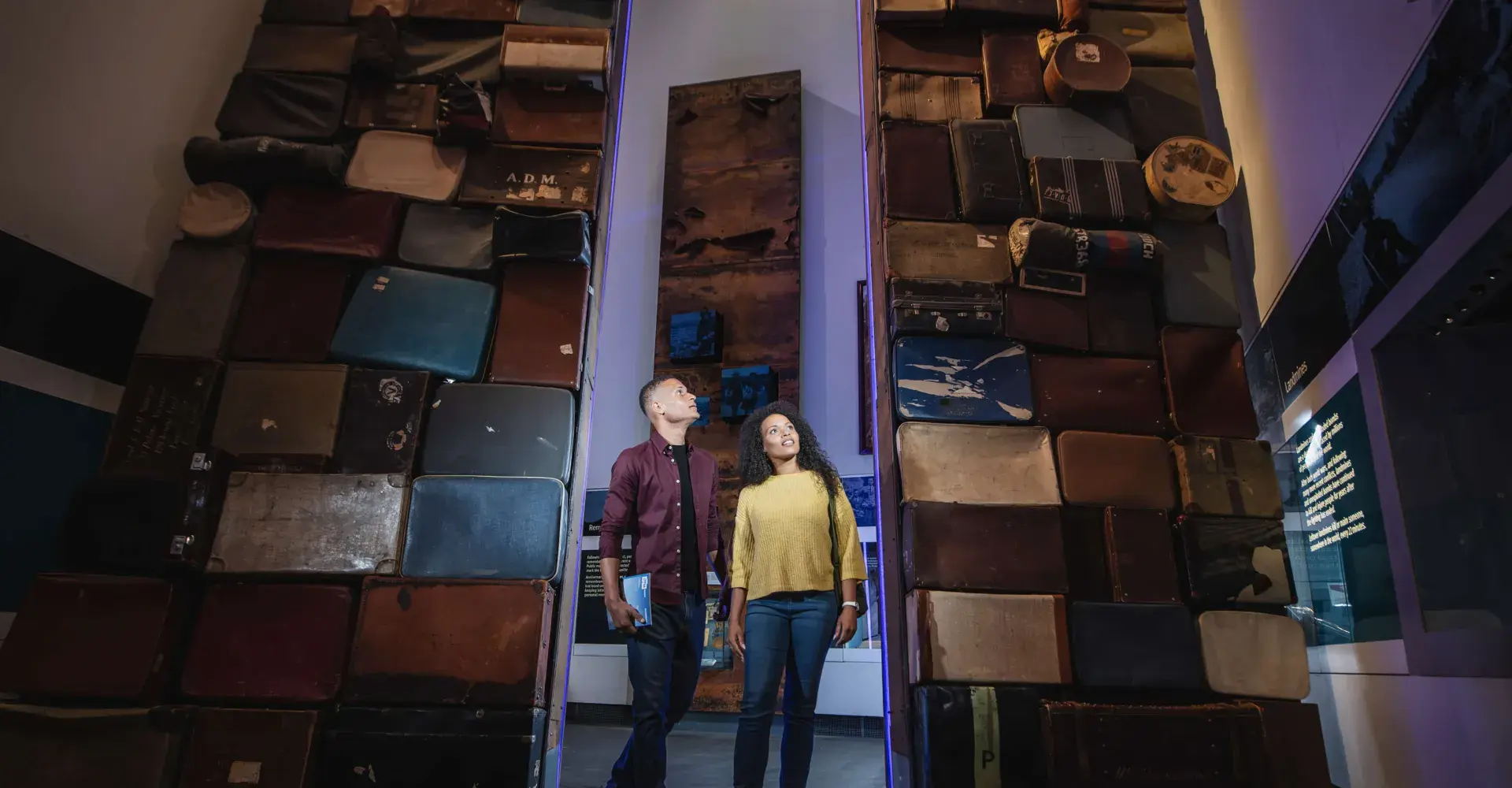 Visitors in the main exhibition hall, IWM North, looking up at a stack of travel cases