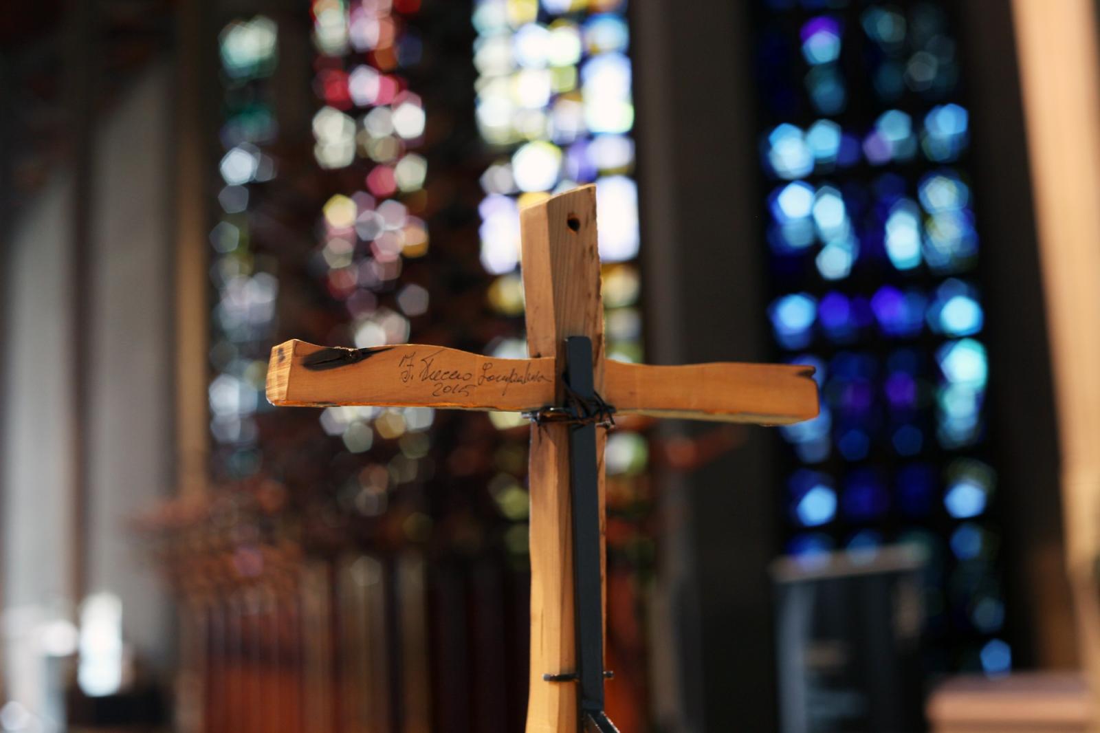 The Lampedusa Cross on display, taken from behind with signature, stained glass window out of focus in background