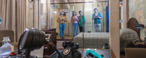 Four people look inside Churchill's Bedroom with his desk in the foreground. They are looking through a glass partition.