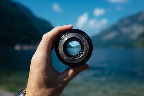 Hand holds camera lens focusing on a lake. (Credit: Unsplash)