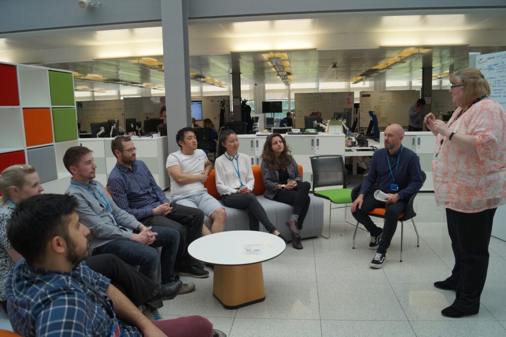 Barbara Price standing talking to a group of attendees who are sitting in a semi circle