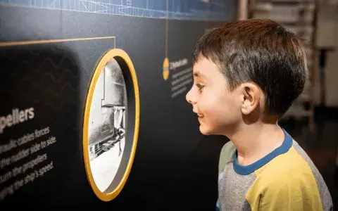Young boy studies porthole shaped display inside HMS Belfast