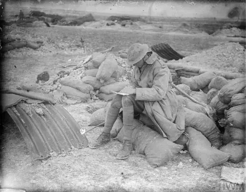 A British officer sat on sand bags writing a letter home on the Western Front, May 1917.