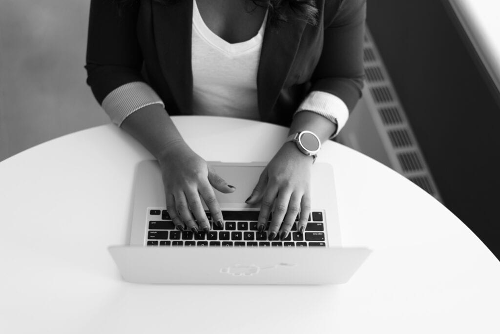 Person sitting a table with laptop, hands and arms in view