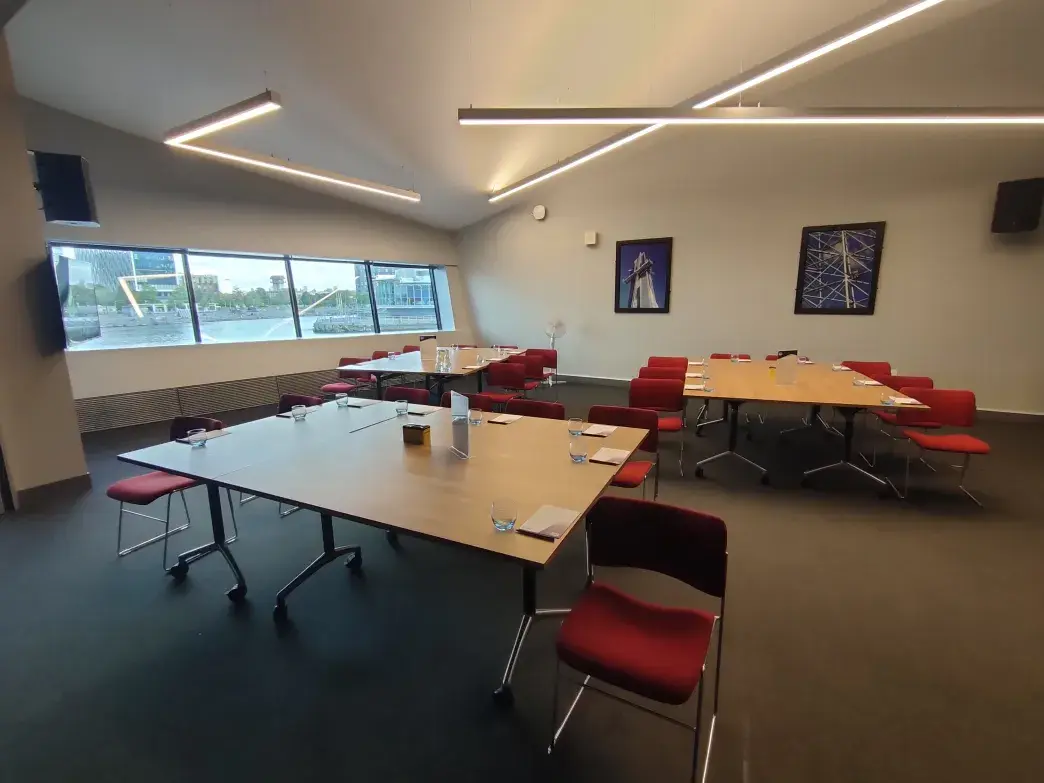 Office space set up with three large tables, red chairs and stationery. 
