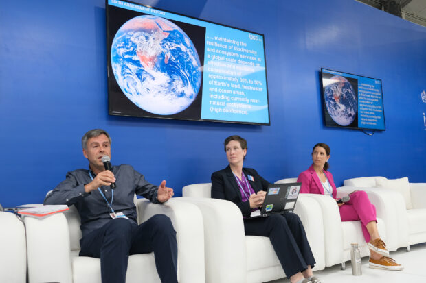 Mike and colleagues discussing Nature-Based Solutions. They are sat on a panel discussion. With large screens behind them