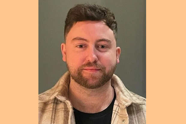 A man with short hair, a beard and wearing a checked shirt.