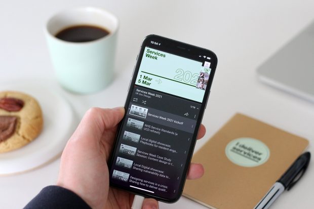 A person holding a smartphone showing a YouTube playlist of Services Week 2021 session recordings