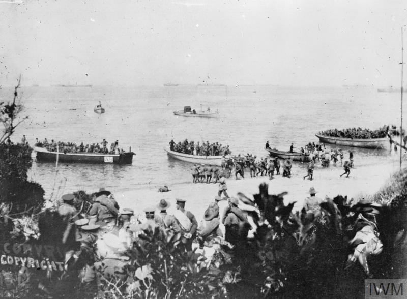 Australians landing at Anzac Cove on 25 April 1915. Troops can be seen arriving on boats, some are waiting on shore.