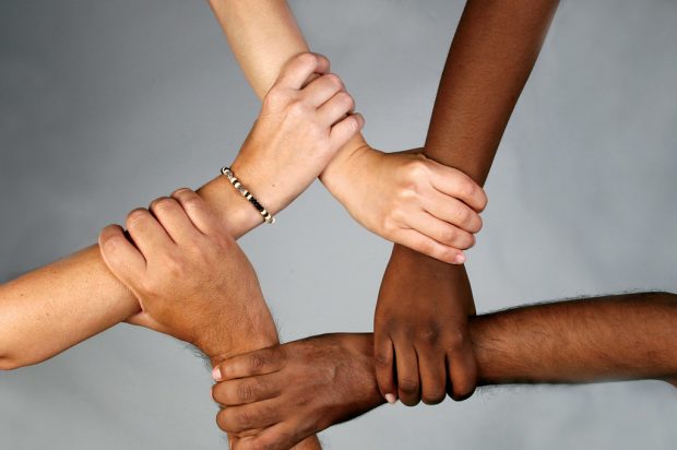 The image shows 5 arms, each holding each other and each with a different skin tone.