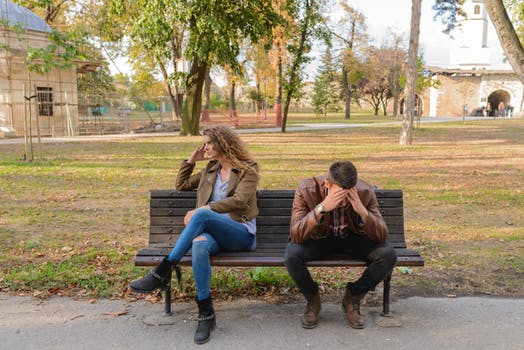 man and woman on bench. Man has head in hands and women is facing the other direction.