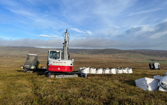 an excavator is on a peatland next to bags of moss ready to be moved.