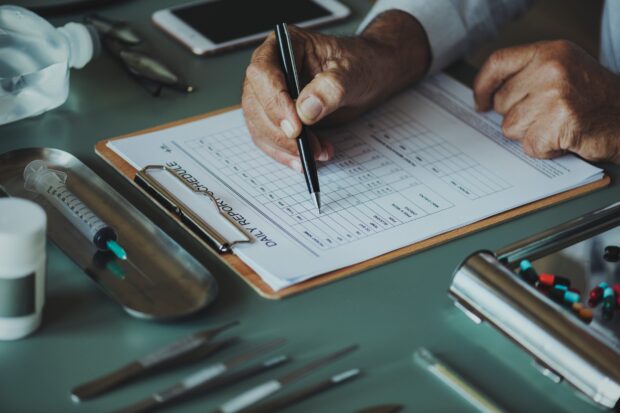 Hand with pen poised over clipboard, representing medical professional completing a report form.