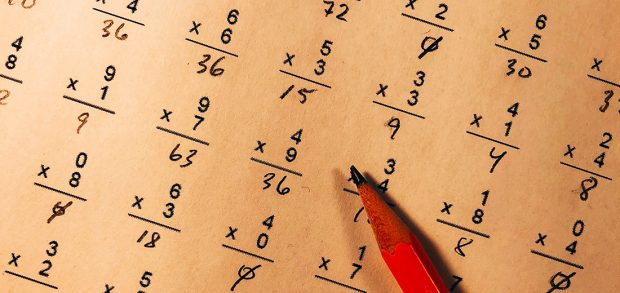 Image shows paper marked up with rows of maths sums with red pencil lying flat on the page