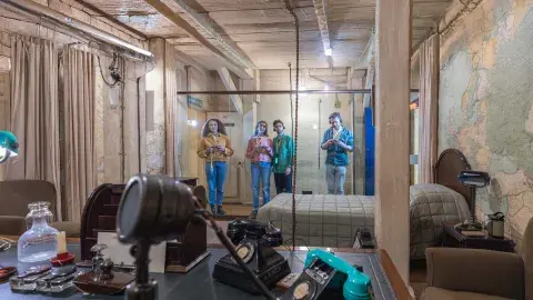 A group of four people stand behind a glass partition, looking into Winston Churchill's bedroom