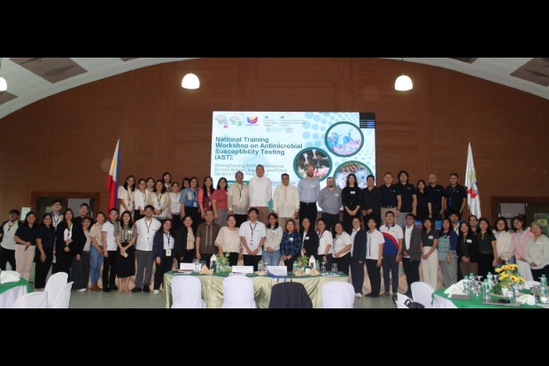 A large group of people standing for a photo against a screen with, "National Training Workshop on Antimicrobial Susceptibility Testing (AST)" displayed.