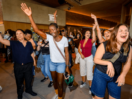 A group of people dancing indoors with their hands up