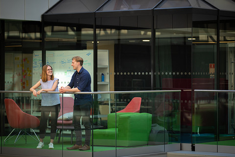 Two individuals standing in front of a green couch, overlooking a balcony