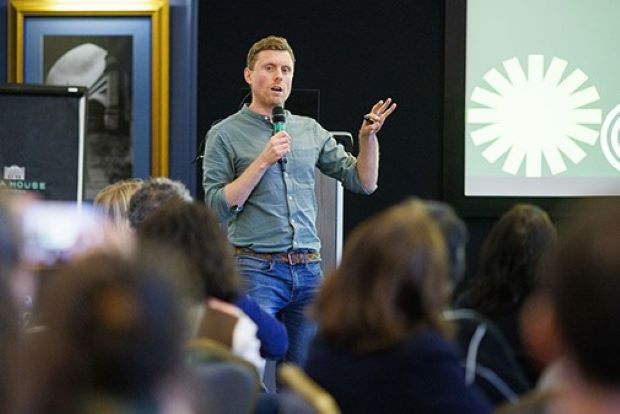 A man with a microphone addressing a room of people.