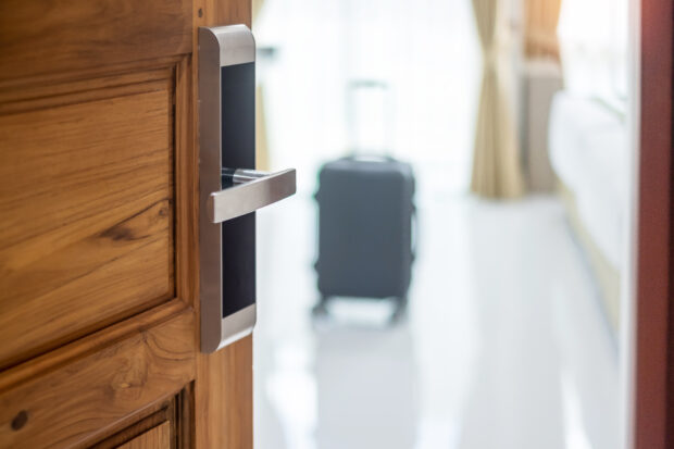A wooden door opening to show a black suitcase next to a white bed.