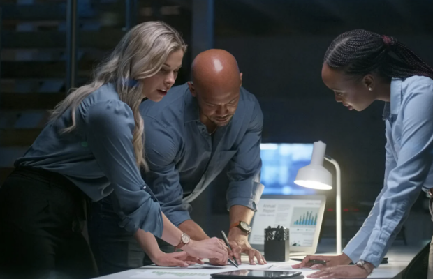 A photo of three people leaning over documents on a desk.
