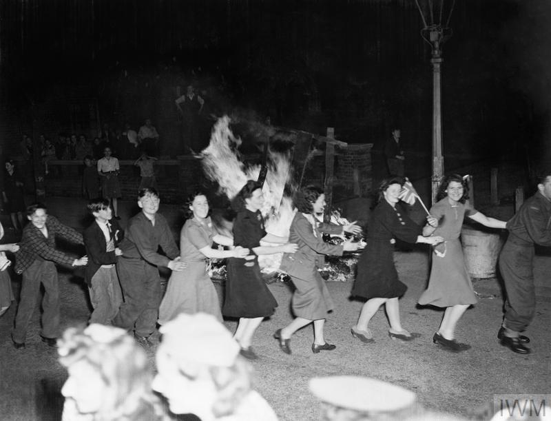 Men and women dance the conga around a bonfire in East Acton, London during the evening of VE Day, 8 May 1945.