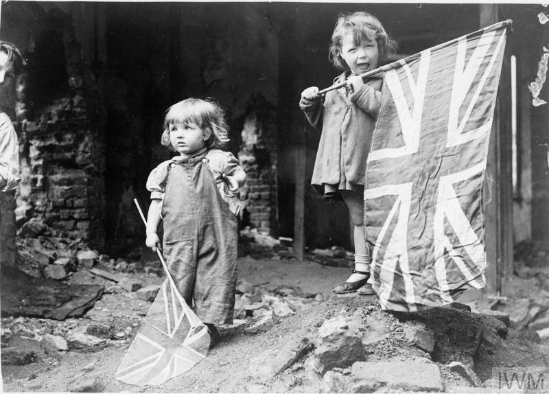Two small girls waving their flags in the rubble of Battersea, snapped by an anonymous American photographer.