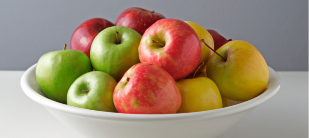 A white bowl containing green, red and yellow apples.