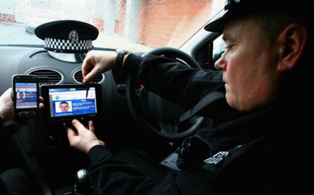A police officer sitting in a police vehicle looking at a digital ID of a person