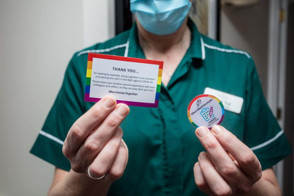 Staff member holds up a vaccination badgevaccina