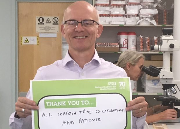 Man holding up a board which says 'thank you to all seafood trial collaborators and patients'.