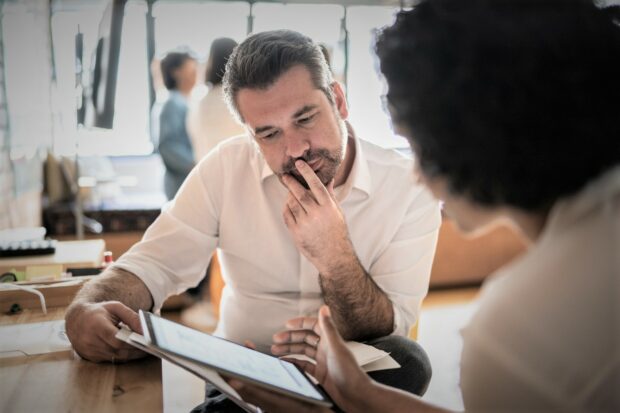A man and woman collaborating over a document on a tablet computer.