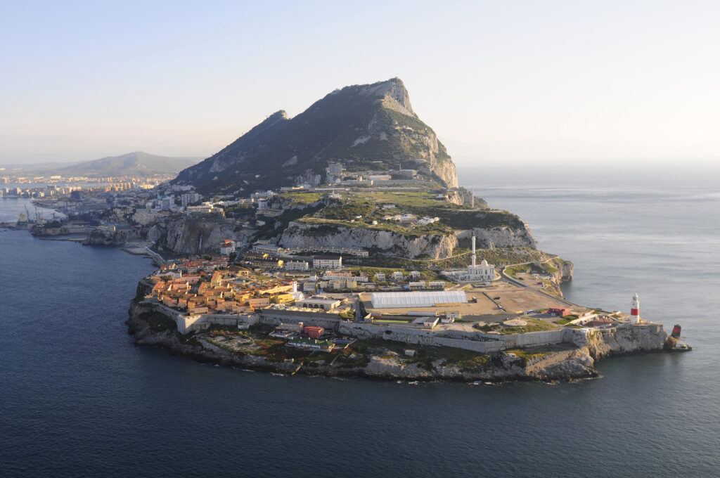 Gibraltar from the air, above the south coast of the peninsula. The Rock takes up most of the background with buildings on the headland in the foreground.