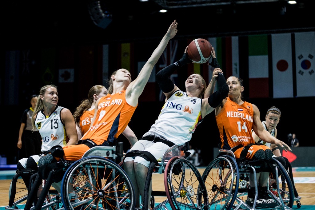 Wheelchair basketball athletes from opposing teams are reaching for the ball