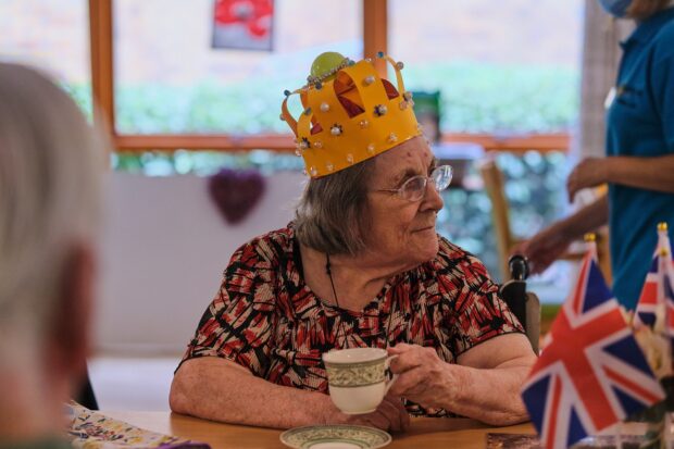 Luke Whittemore Photography Lady sat down holding a cup and wearing a paper made crown decorated in beads and gems.